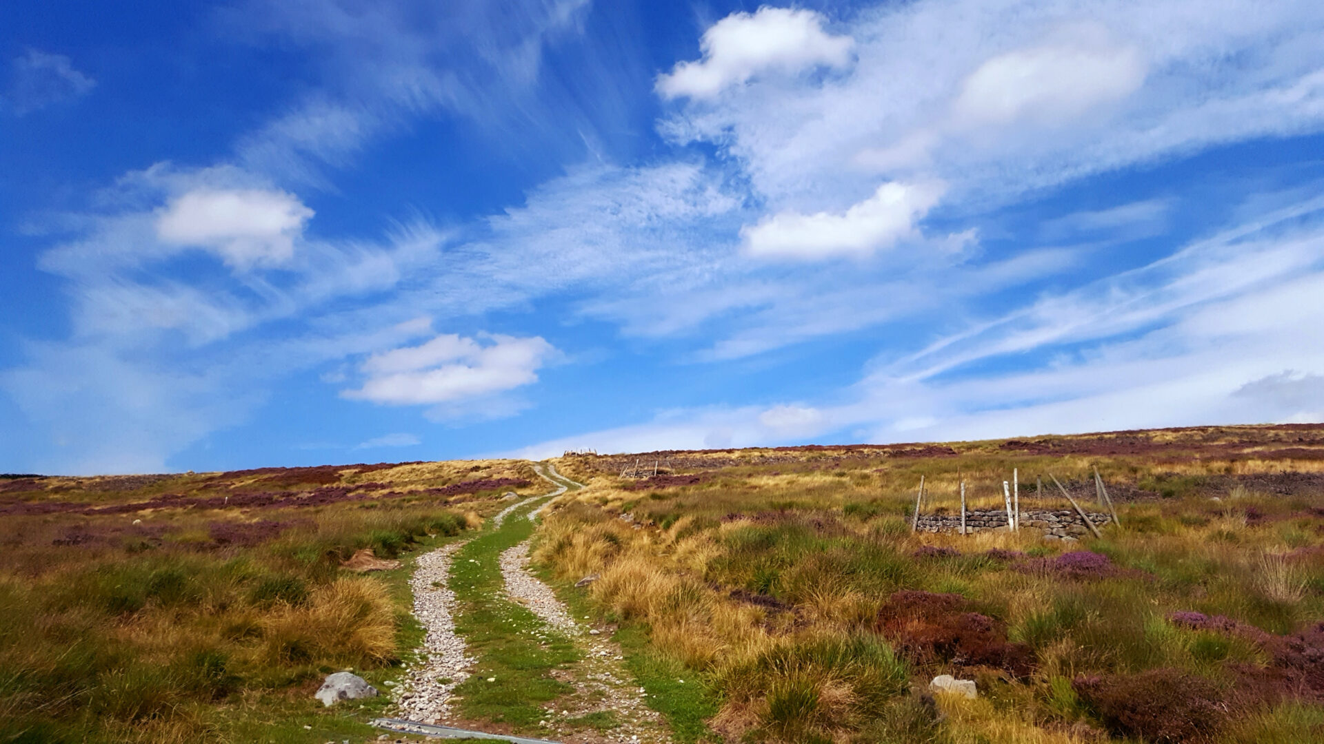 Rough track heading over moorland with blue sky